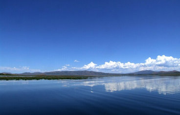 An aerial view of the blue waters of Blackfoot Reservoir with mountains in the far distance on a cloudless blue day near Soda Creek Campground in Soda Springs, Idaho.